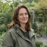 Portret van een vrouw met schouderlang haar in een olijfgroene jas in een tuin