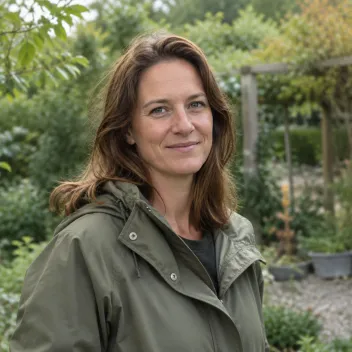 Portret van een vrouw met schouderlang haar in een olijfgroene jas in een tuin